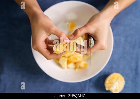 Gros plan sur les mains de la femme caucasienne inconnue séparant les tranches d'orange sur le bol sur la table à la maison - concept de saine alimentation bio homead Banque D'Images