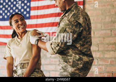 Une femme soldat sourit insouciante à l'infirmière militaire après avoir reçu un rappel de vaccin Covid-19. Militaire américaine ayant un adhésif médical Banque D'Images