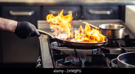 Chef professionnel flamant dans la cuisine dans une poêle à gaz. Banque D'Images