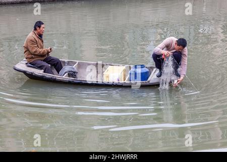 Deux personnes pêchant sur un bateau à fond plat dans une voie navigable de Jiashan, en Chine Banque D'Images
