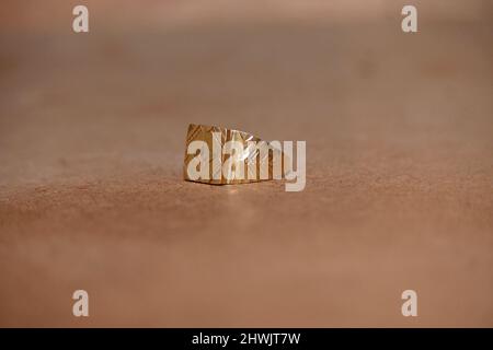 gros plan la belle bague dorée garder sur la table brune sur un arrière-plan rouge marron hors foyer. Banque D'Images