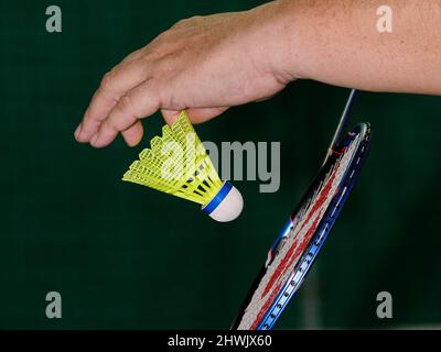 Gros plan d'une main tenant un volant au-dessus d'une raquette de badminton, capturant un moment sportif en salle concentré. Banque D'Images