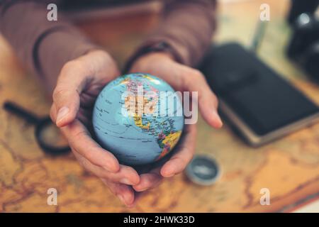 Globe, monde entier entre les mains et boussole, loupe et livre sur la carte d'itinéraire sur la table. Voyage , aventure et découverte concept. Banque D'Images