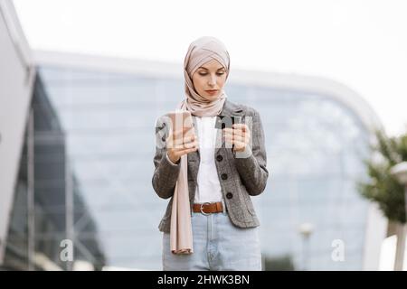 Jolie dame musulmane dans hijab utilisant un smartphone et une carte de crédit pour les achats en ligne. Femme d'affaires focalisée sur le port du foulard dans la rue et sur l'achat. Banque D'Images