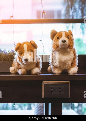 Une jolie poupée de chiens blancs et bruns s'assoit sur le comptoir près d'une grande fenêtre en verre dans le café. Belle décoration de jouets animaux dans le café. Magnifiques chiens de poupée dans br Banque D'Images