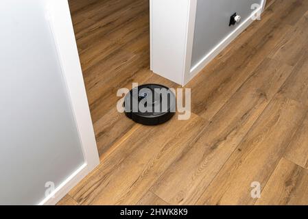 Un aspirateur robot moderne fonctionnant sur des panneaux en vinyle, un robot de nettoyage autonome. Banque D'Images