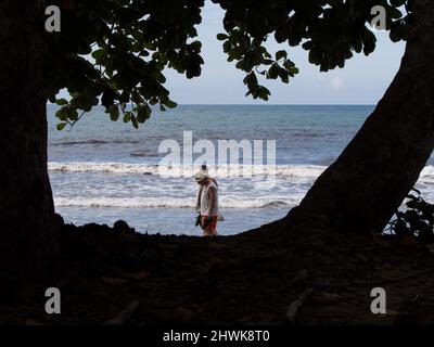 Silhouette de deux grands arbres qui encadrent deux personnes marchant sur une plage des Caraïbes au Costa Rica. Banque D'Images