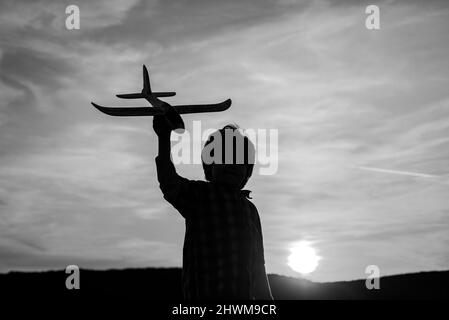 Petit garçon volateur au coucher du soleil. Petits enfants avec un avion jouet dans un champ au coucher du soleil. Le succès et le concept de chef d'enfant. Banque D'Images