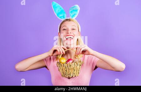 Le jour de Pâques. Fille souriante aux oreilles de lapin avec panier d'œufs de couleur. Femme lapin. Vacances de printemps. Banque D'Images