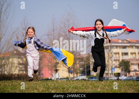 Belles petites filles avec des drapeaux ukrainiens et russes en cours de course heureux dans le parc. Concept de paix entre le peuple ukrainien et le peuple russe Banque D'Images