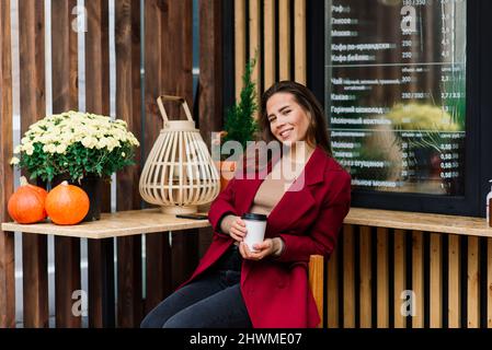 Une femme heureuse dans un café en plein air qui boit et sourit Banque D'Images