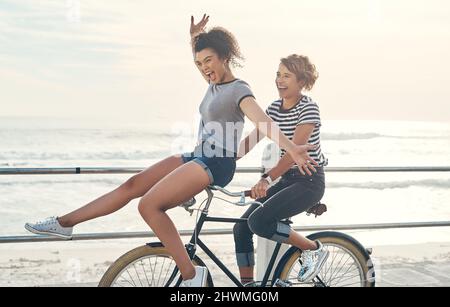 Nous ne disons jamais non aux aventures sauvages. Photo de deux amis qui s'amusent à faire du vélo le long de la côte. Banque D'Images