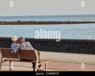 couple âgé assis sur un banc en face de la mer avec un masque Banque D'Images