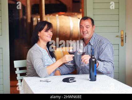 À notre avenir. Un heureux couple mature qui toaster avec un peu de vin rouge tout en étant assis à une table sur une cave à vin. Banque D'Images