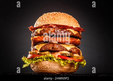 Double hamburger avec bacon grillé fromage jaune oignons tomates concombres et laitue. Isolé sur fond noir. Banque D'Images