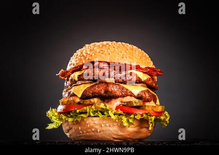 Double hamburger avec bacon, fromage, oignons, tomates, concombre et laitue. Isolé sur fond noir. Banque D'Images