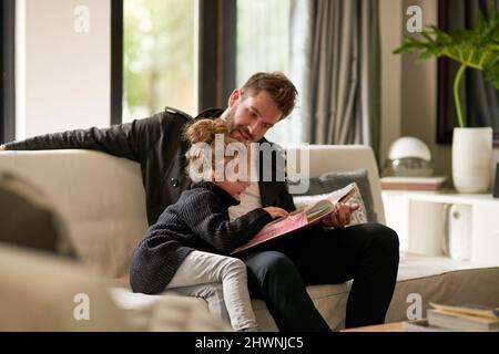 Rien de mieux que d'être à l'ambiance intime avec un livre ensemble. Photo rognée d'un père lisant une histoire à sa fille à la maison. Banque D'Images