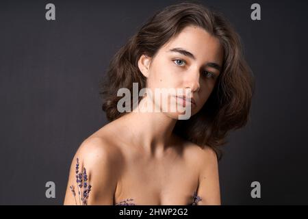 Concept d'aisselle non rasé. La fille tient des fleurs de lavande devant ses aisselles. Symbole des parties du corps non rasées. Positivité et naturel du corps. Problèmes d'épilation à la maison sur fond noir Banque D'Images