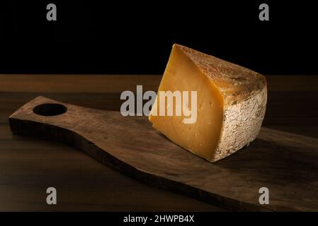 Morceau d'un fromage Kars sur une planche à découper en bois et fond noir avec un espace de copie. Banque D'Images