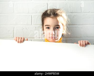 Une fille triste tient une feuille blanche de papier - maquette pour la publicité, le slogan, l'inscription. L'espace de copie est entre les mains des enfants, l'enfant est contrarié et caché Banque D'Images