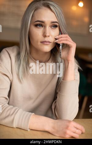 Photo verticale de calme contrarié déçu perplexe belle femme blonde, propriétaire café, téléphone parlant. Week-end de travail Banque D'Images