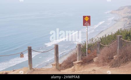 Falaise instable abrupte, roche ou bluff, temps brumeux, érosion de la côte de Californie, États-Unis. Le crag érodé de Torrey Pines donne sur le point de vue, les vagues de l'océan d'en haut. Garde-corps de chaîne pour trekking de sécurité, signe de danger. Banque D'Images