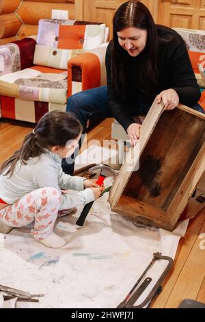 Petite fille avec un marteau dans les mains fixant l'ancienne boîte en bois et la mère tenant la boîte fermement dans l'atelier pour la rénovation. Donner une vie nouvelle aux choses anciennes. Réutilisation de Banque D'Images