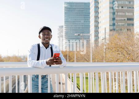 Jeune homme souriant avec téléphone mobile en ville Banque D'Images