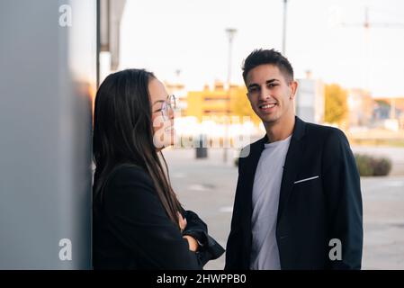 Homme d'affaires souriant par un collègue penché avec les bras croisés sur le mur Banque D'Images