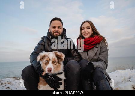 Jeune couple souriant assis avec un chien à la plage Banque D'Images