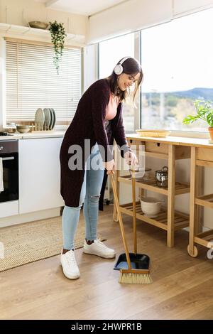 Femme nettoyant le sol avec un balai et une pelle à poussière dans la cuisine à la maison Banque D'Images