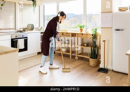 Une jeune femme nettoie le sol de la cuisine avec un balai à la maison Banque D'Images