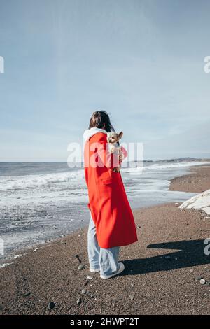 Femme transportant un chien debout près de la mer à la plage Banque D'Images