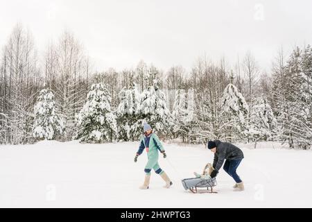 Père poussant sa fille sur un traîneau par une femme marchant sur la neige en hiver Banque D'Images