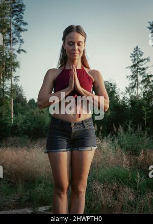 Femme méditant avec les mains jointes dans la forêt Banque D'Images