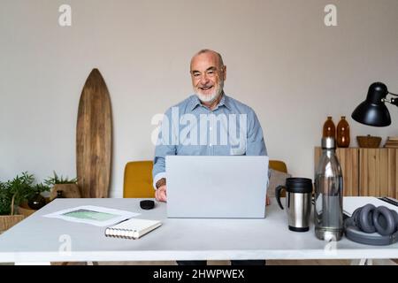Homme d'affaires expérimenté heureux assis avec un ordinateur portable au bureau Banque D'Images