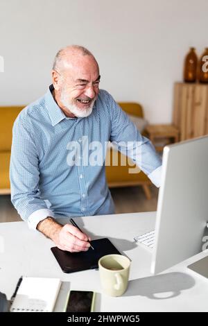 Homme d'affaires joyeux avec une tablette graphique regardant l'ordinateur dans le bureau à domicile Banque D'Images
