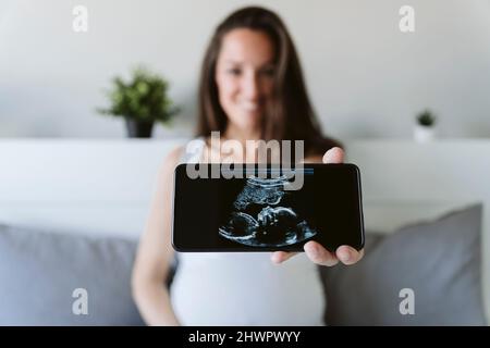 Femme montrant une échographie par téléphone portable à la maison Banque D'Images