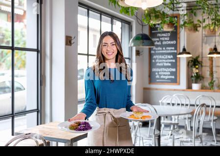 Serveuse souriante transportant des assiettes à nourriture dans le café Banque D'Images