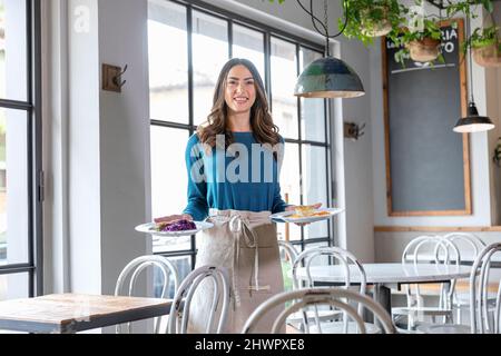 Serveuse souriante avec des assiettes à manger au café Banque D'Images