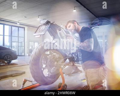 Jeune mécanicien examinant le tuyau d'échappement de la moto en atelier Banque D'Images