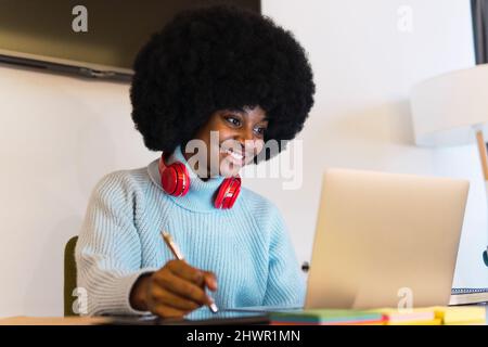 Femme afro souriante regardant un ordinateur portable et travaillant sur un bureau Banque D'Images