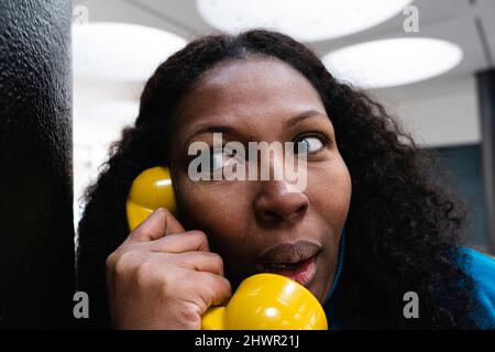 Curieuse femme à l'écoute à travers le vieux récepteur de téléphone jaune Banque D'Images