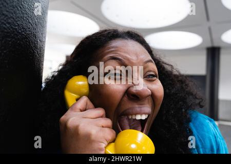 Bonne femme à l'écoute par un ancien récepteur de téléphone jaune Banque D'Images