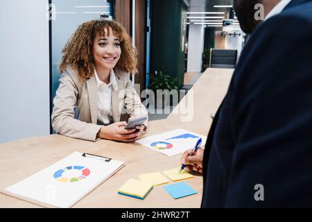 Collègue souriant regardant un homme d'affaires travaillant au bureau de collègue Banque D'Images