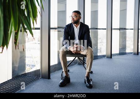 Un jeune homme d'affaires aux mains clased assis sur une chaise au bureau Banque D'Images