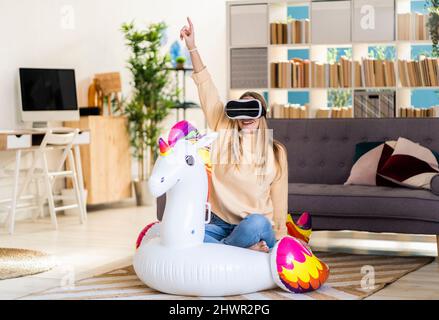 Jeune femme portant des lunettes VR sur une licorne gonflable dans le salon Banque D'Images