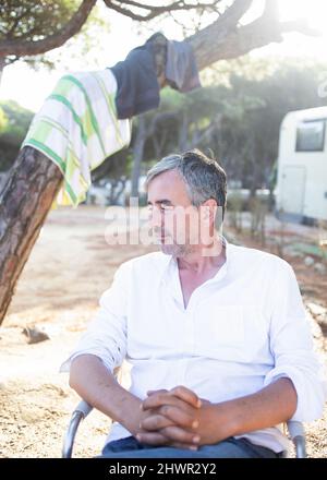 Homme assis avec les mains clappées sur la chaise au camping Banque D'Images