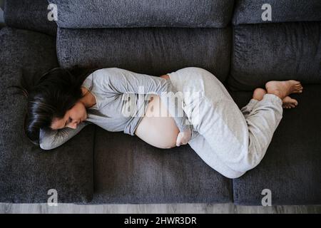 Femme enceinte couchée sur un canapé à la maison Banque D'Images
