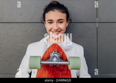 Femme souriante avec planche à roulettes devant le mur noir Banque D'Images